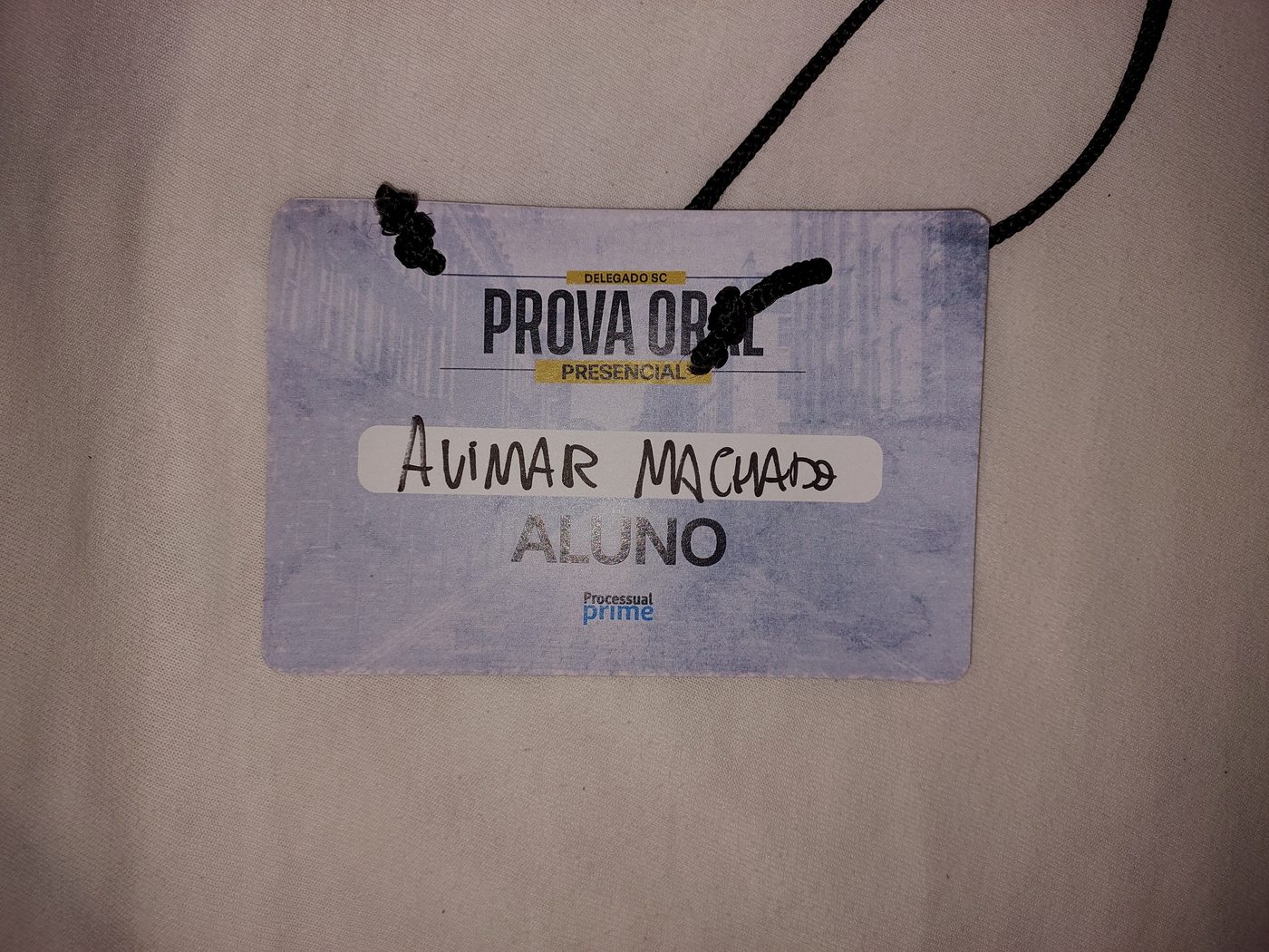 Crachá de identificação escrito 'Prova Oral Presencial — Aluno — Avimar Machado', do simulado da prova oral da PCSC.