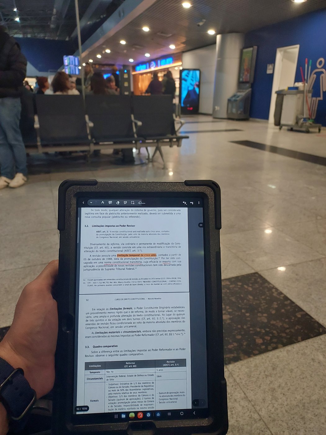Avimar estudando material jurídico no tablet, sentado dentro de um aeroporto.