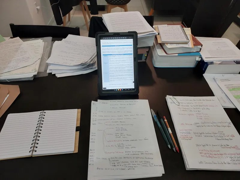 Mesa coberta de resumos escritos à mão e um tablet, na véspera da prova oral da PCSC.